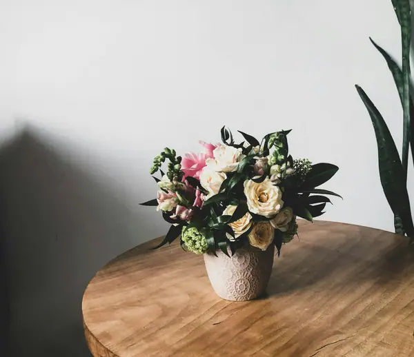 Garden-style arrangement of roses in a white pot on a round wooden table