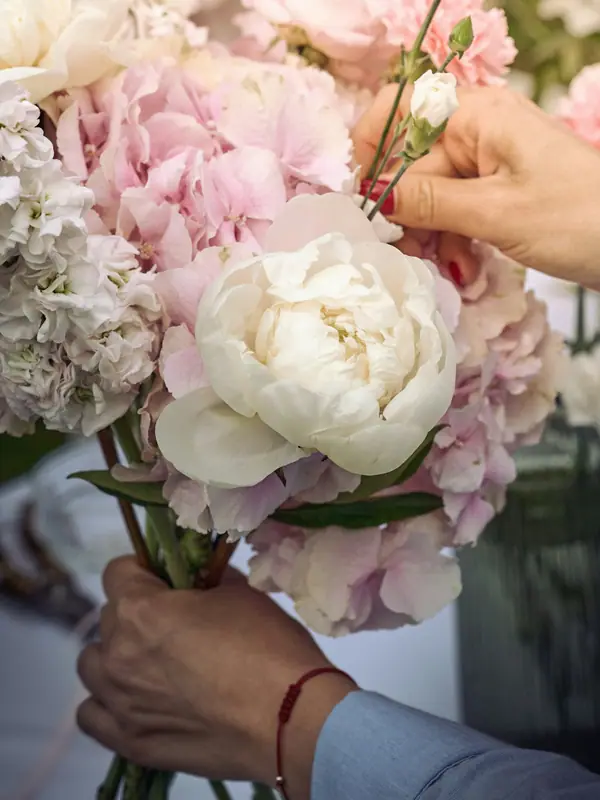 Hands arranging a bouquet of blush and white peonies