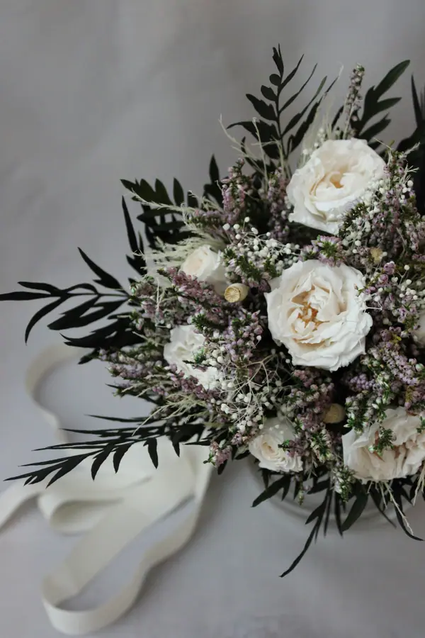 Bouquet of white roses, heather and dark foliage tied with ribbon