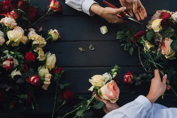 Hands trimming roses on a dark worktable